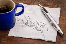 Connecting puzzle pieces on white napkin with a cup of coffee